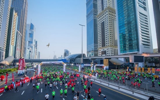 Ampia strada a più corsie riempita di corridori per la Dubai Run tra i moderni grattacieli della città